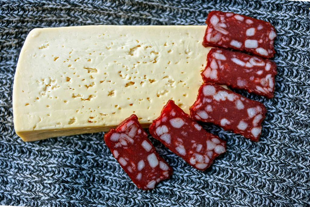rebanando salchichas rojas de salami y un trozo de queso en tela gris
 - Foto, Imagen