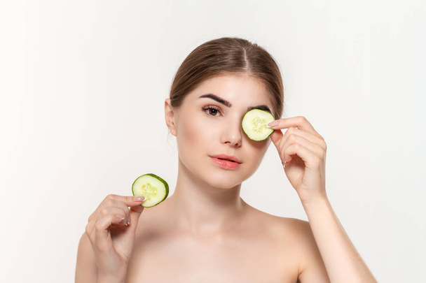 Close-up portrait of a beautiful young girl holding slices of  green cucumber close to eyes isolated over white background. - Photo, image