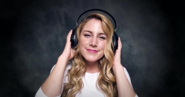 Beautiful blonde listens to music on headphones on a dark background. - Footage, Video
