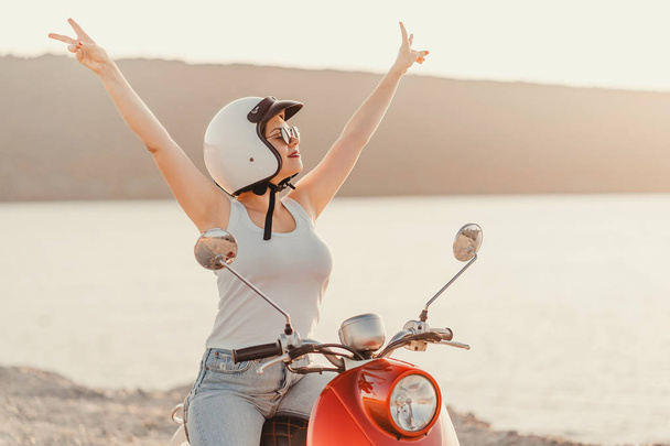 Happy girls portrait with open and up peace sign hands. Lady in white clothes and helmet sitting on red retro moped at sunset river background. - Φωτογραφία, εικόνα