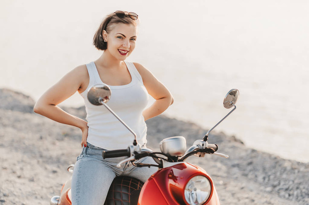 Attractive girls portrait. Lady in white clothes sitting on red retro moped at sunset background. Travel concept. - Foto, imagen