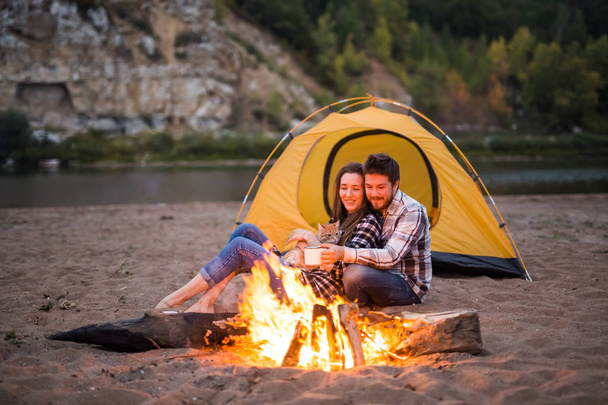 People, tourism and nature concept - Man embrace woman sitting near a fire - Photo, Image