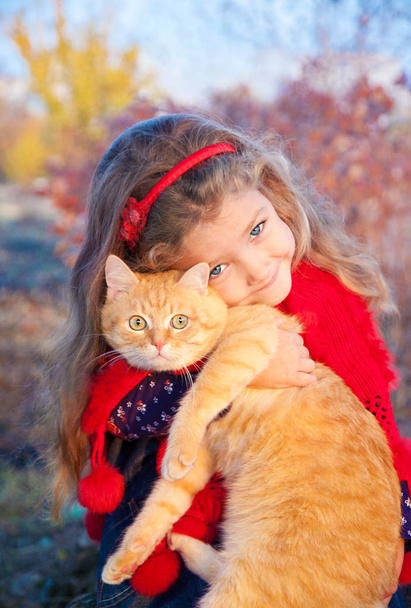 Portrét malé holčičky s červeným kocourem v dlaních na podzim. - Fotografie, Obrázek