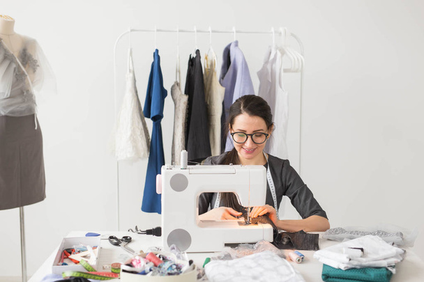 Krawieckie, krawiec i moda koncepcja - uśmiechający się kobiece projektant mody, przy użyciu maszyny do szycia i siedzi za biurkiem jej - Zdjęcie, obraz