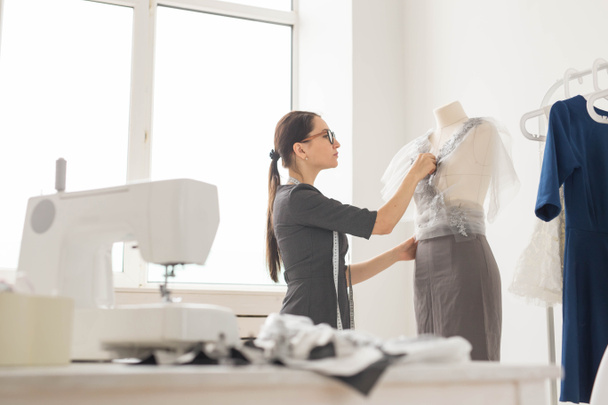 Naaister, kleermaker, mode en showroom concept - zijaanzicht van vrouwelijke mode-ontwerpster meten van materialen op etalagepop in kantoor - Foto, afbeelding