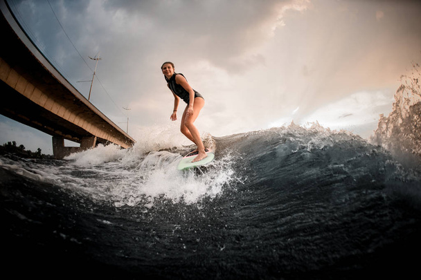 Sportowa dziewczyna stoi na wakeboard na rzece w tle mostu - Zdjęcie, obraz