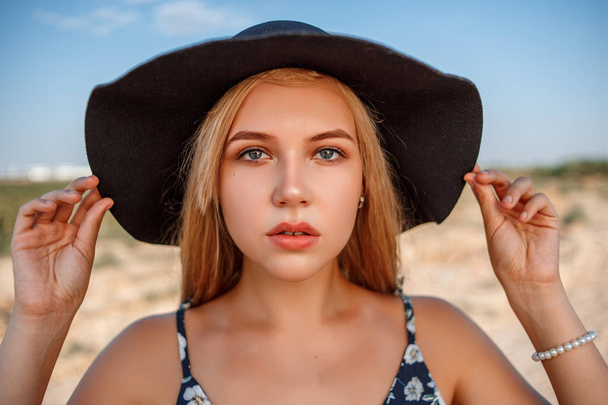 a close-up portrait of a blue-eyed blonde girl in a black hat an - Photo, image