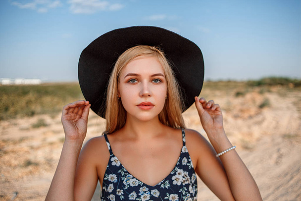 ένα κοντινό πορτραίτο ενός γαλάζιου ξανθού κοριτσιού με ένα μαύρο καπέλο - Φωτογραφία, εικόνα
