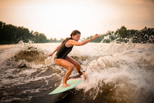 Woman making a trick on the green wakeboard on the river in the sunset - Foto, imagen