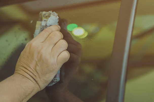 Close-up bij de hand van mannelijke werknemer natte kranten gebruiken om het glas gedeelte van de auto te reinigen - Foto, afbeelding