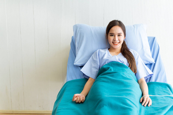 Asyalı genç bayan hastalar mavi gömlekler giyip parlak yüzlü yatakta yatıyorlar. Doktorun kontrol etmesini beklerken daha iyi semptomlar gösteriyorlar. - Fotoğraf, Görsel