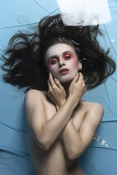 A beautiful naked girl with conceptual makeup in red tones is la - Foto, imagen