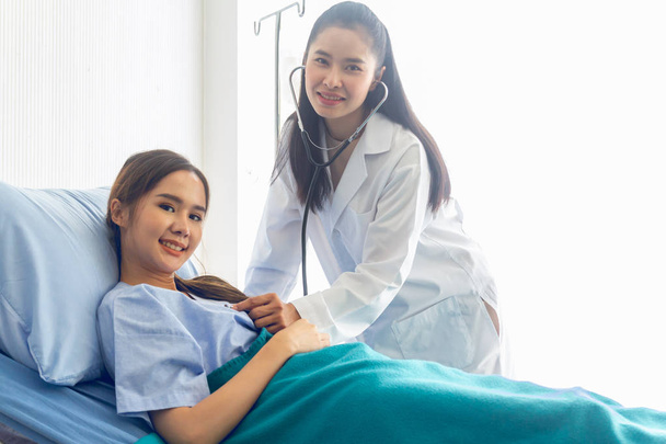 ベッドに横たわるアジアの若い女性患者は、医師が治療結果をチェックし、記録することができます - 写真・画像