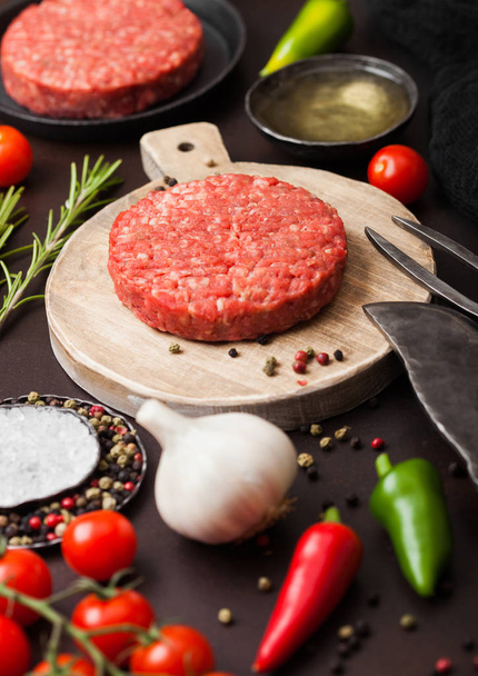Fresh raw minced homemade farmers grill beef burger on round chopping board with spices and herbs and fork and knife on brown board. Oil, pepper and garlic. - Fotoğraf, Görsel