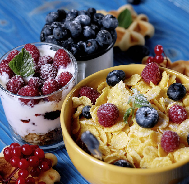 Healthy breakfast with corn flakes, berries, waffle and milk on blue background. - Photo, image
