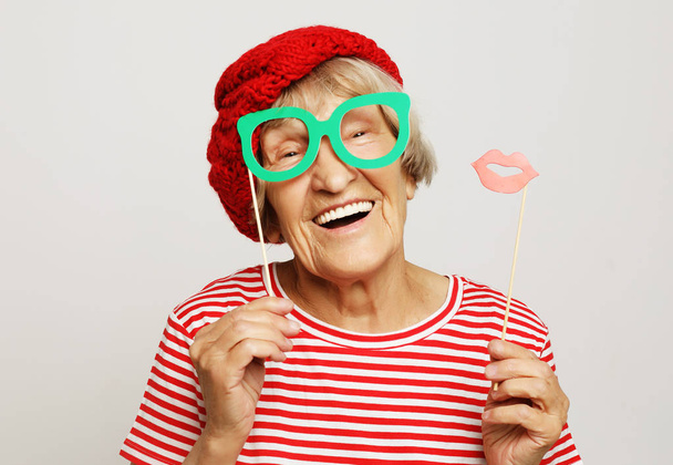 funny grandmother wearing red clothes holding falce glasses and ready for party - Фото, изображение