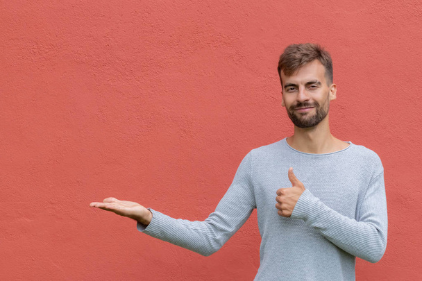Hombre sonriente guapo que finge sostener un objeto o una cosa en el fondo de la pared roja. Copiar espacio para publicidad y texto
. - Foto, imagen