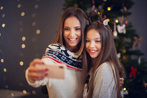 Mother and daughter celebrating Christmas at home and taking selfie - Photo, Image