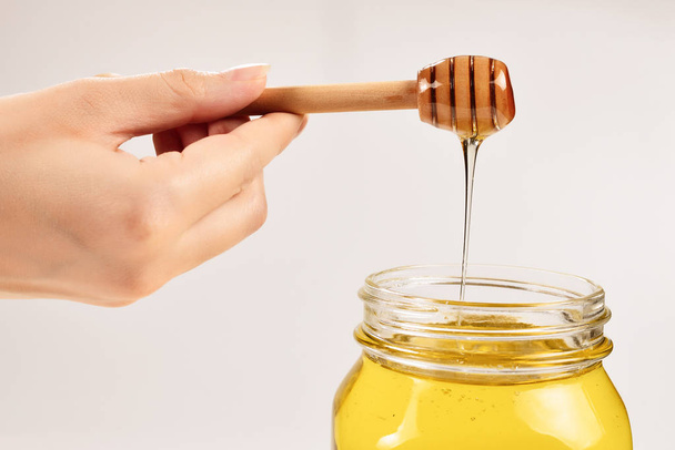 Dipper met honing in de hand van een vrouw. Ruimte voor tekst of ontwerp.  - Foto, afbeelding