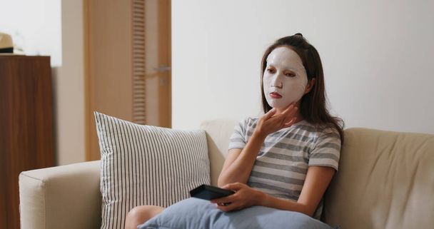Vrouw van toepassing gezichtsmasker en tv kijken thuis - Foto, afbeelding