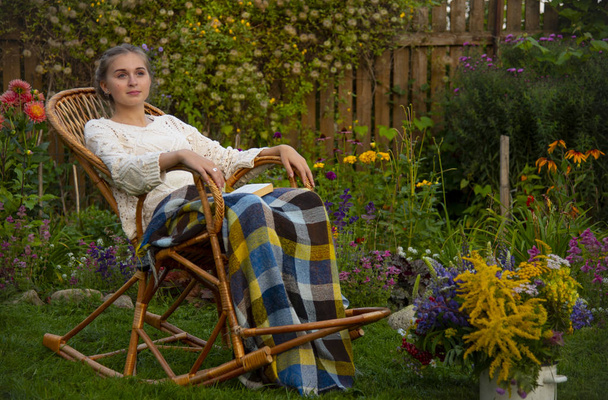 Beautiful girl sitting in a wicker rocking chair with a book - Photo, image