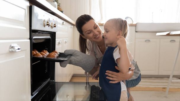 Little girl and beautiful mother taking muffins out the oven - Foto, Imagem
