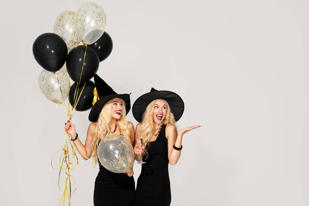 portrait of two happy young women in black witch halloween costumes with balloons on party over white background. the concept of Halloween . funny faces - Photo, Image