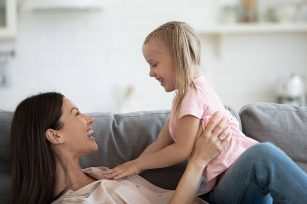 Jovial mother playing with little daughter lying on couch - Photo, Image