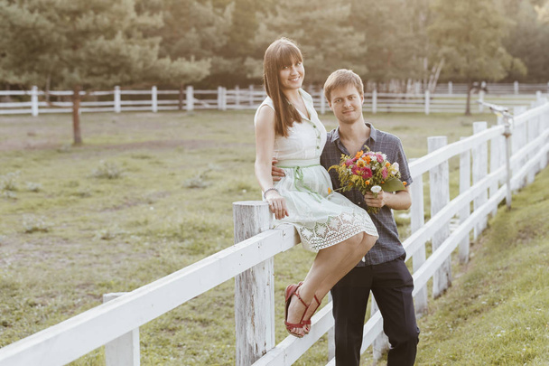 De bruidegom maakt een aanbod aan de bruid, de betrokkenheid van twee jonge mensen. Mooi meisje in een zomer jurk met een boeket in haar handen in het Park - Foto, afbeelding