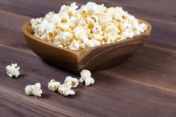 Popcorn in a brown wooden plate in the shape of a heart on a wooden table. Popcorn is laid out on the table - Φωτογραφία, εικόνα