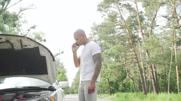 Hombre africano guapo llamando al servicio de remolque en la carretera rural
 - Metraje, vídeo