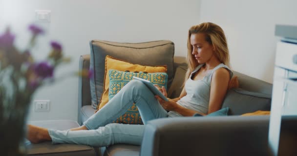 Υψηλής ποιότητας βίντεο 12bit του όμορφο κορίτσι χρησιμοποιώντας tablet PC κάθεται στον καναπέ στο σπίτι. Γυναίκα σέρφινγκ ιστού, κοινωνικά δίκτυα, ψάχνει κάτι στο online κατάστημα. - Πλάνα, βίντεο
