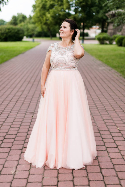 公園で遠ざかるエレガントな床長ピンクのドレス夢のブルネットの白人モデル. - 写真・画像
