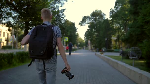 Ένας μαθητής φωτογράφος περπατά κατά μήκος ενός δρόμου της πόλης πίσω του - Πλάνα, βίντεο