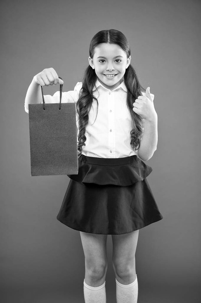Thumbs up for sale. Cute small child showing ok sign to purchase bought at sale on orange background. Happy little girl holding shopping bag after seasonal sale. Shop discounts and deals on sale - Фото, изображение