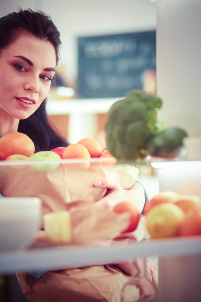 Χαμογελώντας γυναίκα λαμβάνοντας ένα φρέσκο φρούτο από το ψυγείο, έννοια υγιεινής διατροφής - Φωτογραφία, εικόνα
