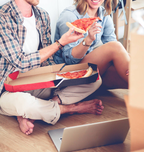 Young couple have a pizza lunch break on the floor after moving into a new home with boxes around them. Young couple - Foto, imagen