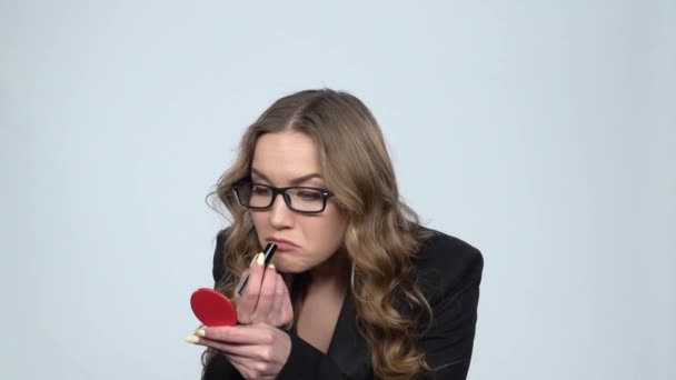 Beautiful woman in glasses paints her lips looking in red mirror, slow motion - Felvétel, videó