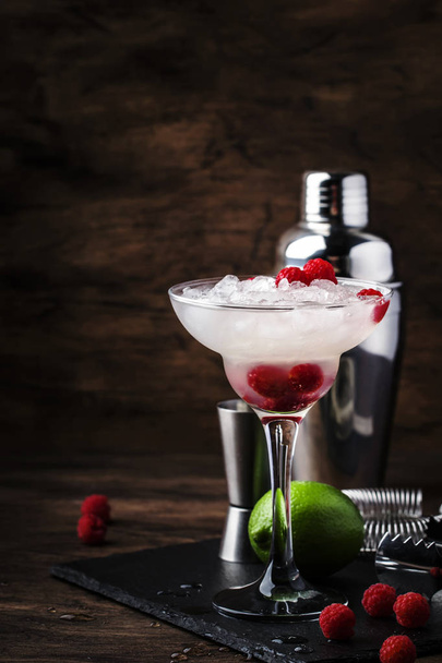 Raspberry daiquiri, alcoholic cocktail with white rum, lime juice, raspberries and crushed ice in tall glass, on wooden bar counter  with steel bar tools - Фото, зображення