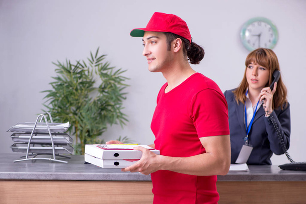 Young male courier delivering pizza to hotels reception  - 写真・画像