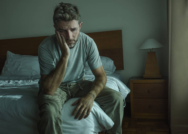 dramatic lifestyle portrait of 30s to 40s handsome man sitting sad on bed feeling worried and desperate suffering depression problem  - Foto, Imagen