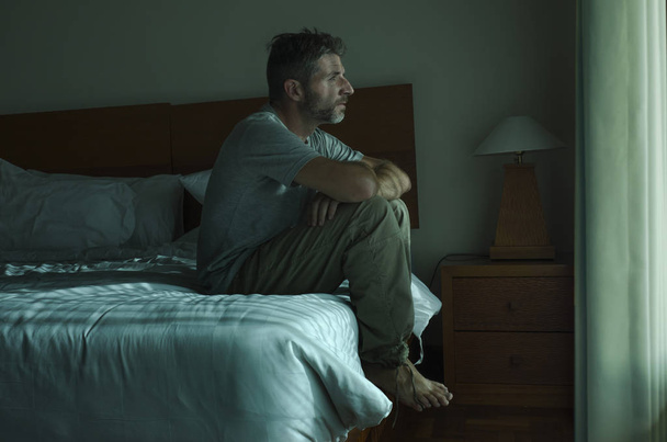 dramatic lifestyle portrait of 30s to 40s handsome man sitting sad on bed feeling worried and desperate suffering depression problem  - Photo, image