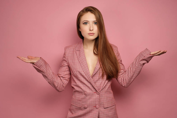 Redhead girl in a jacket stands on a pink background with arms outstretched to the sides and wide-open eyes looking at the camera - Fotoğraf, Görsel