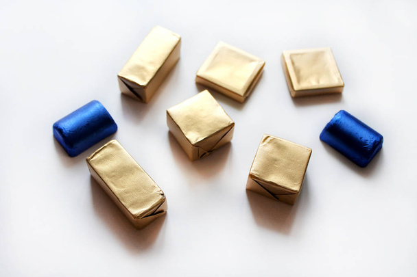Шоколадные конфеты, завернутые в голубую и золотую фольгу, изолированные на белой поверхности
 - Фото, изображение