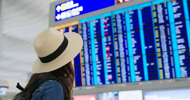 Mujer mira la tabla de horarios en el aeropuerto
 - Foto, Imagen