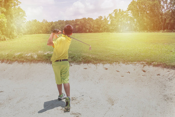 Young Asian Sporty man golfer player doing golf swing tee off on the green evening time - Photo, Image