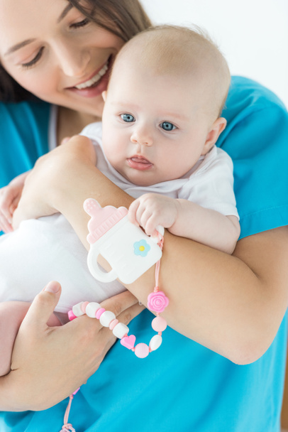 attraente e sorridente madre che tiene in braccio il suo bambino con giocattolo in ospedale
  - Foto, immagini