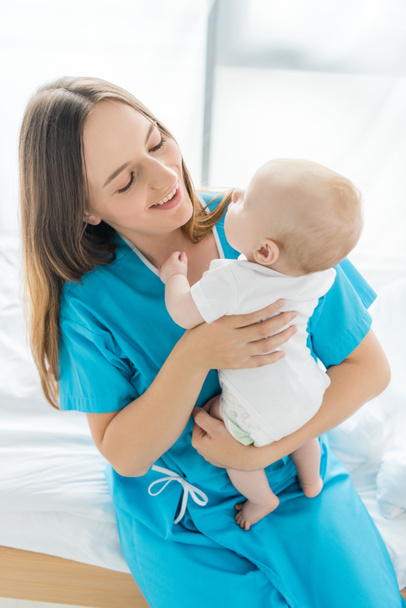 attraente e sorridente madre che tiene il suo bambino in ospedale
  - Foto, immagini
