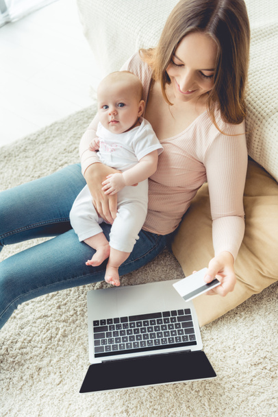 attractive mother holding her child and credit card in apartment  - Фото, зображення