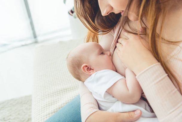 cropped view of mother breastfeeding her child in apartment  - Photo, Image